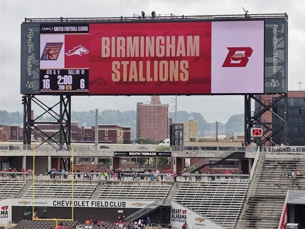 view of Protective Stadium scoreboard at a Birmingham Stallions football, with Birmingham skyline in the background